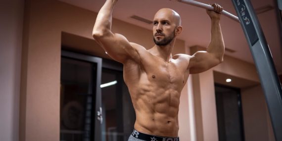 A bald, muscular man performing exercise on gym equipment indoors.